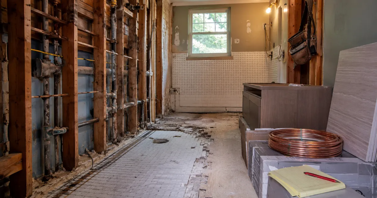 Bathroom mid-renovation showing exposed plumbing and partially demolished walls with new materials nearby